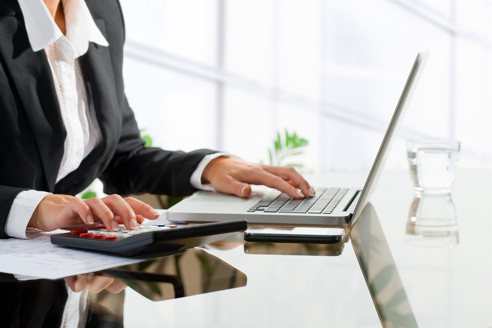 Hands on a calculator and laptop keyboard at a bright desk